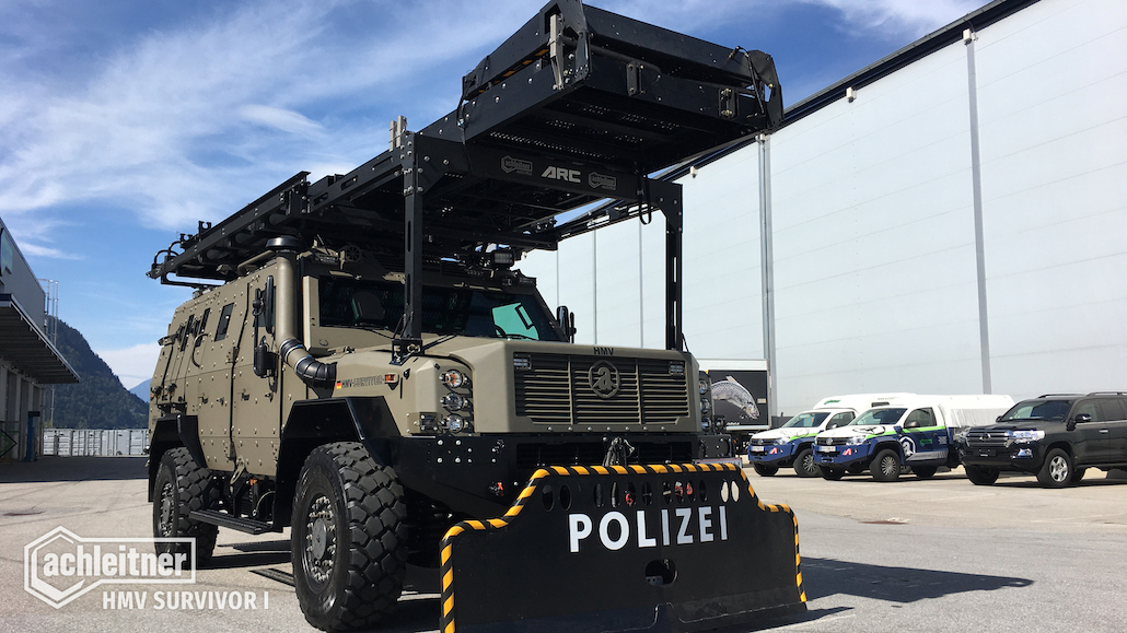 Image shows a khaki green military 4x4 vehicle, the HMV Survivor I, parked in an empty industrial car park.